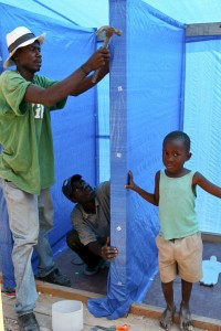 Bou Brun, 7, watches as carpenters use tarpaulins to create walls around the latrines constructed by World Vision in a displacement camp in Port-au-Prince. Photo courtesy of Madeline Wilson, World Vision.